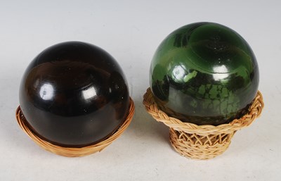 Lot 17 - Two glass floats set on wicker baskets, one...